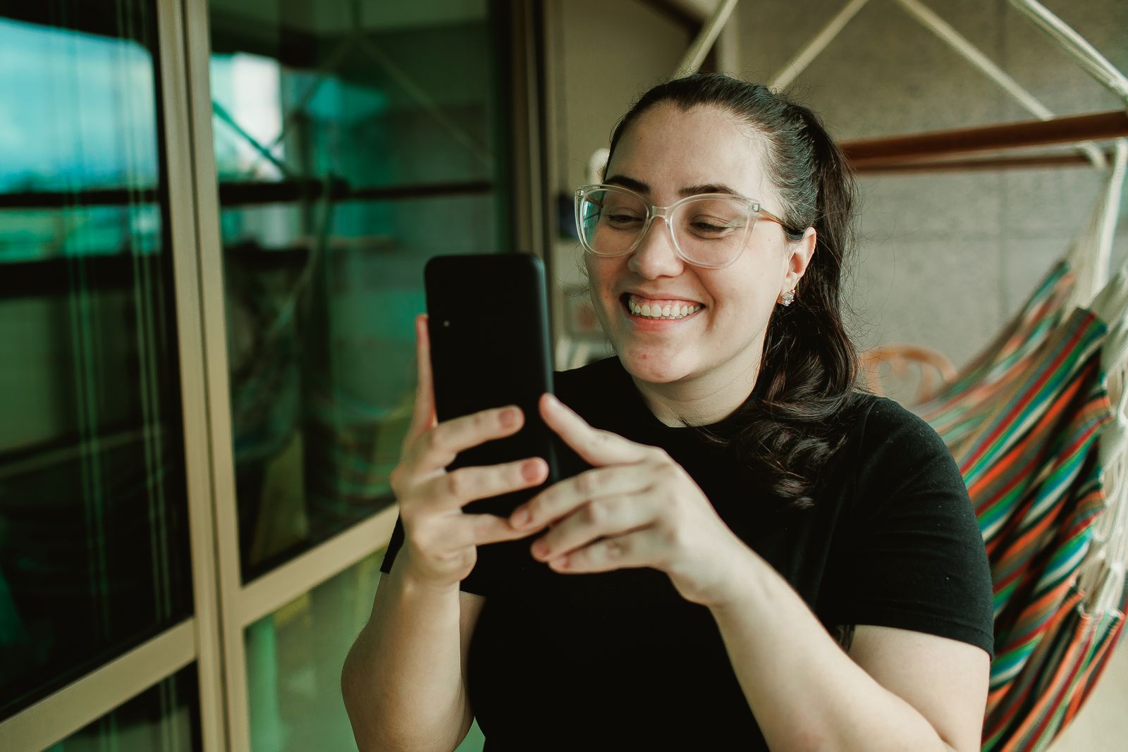 A smiling person using an app on their smartphone indoors