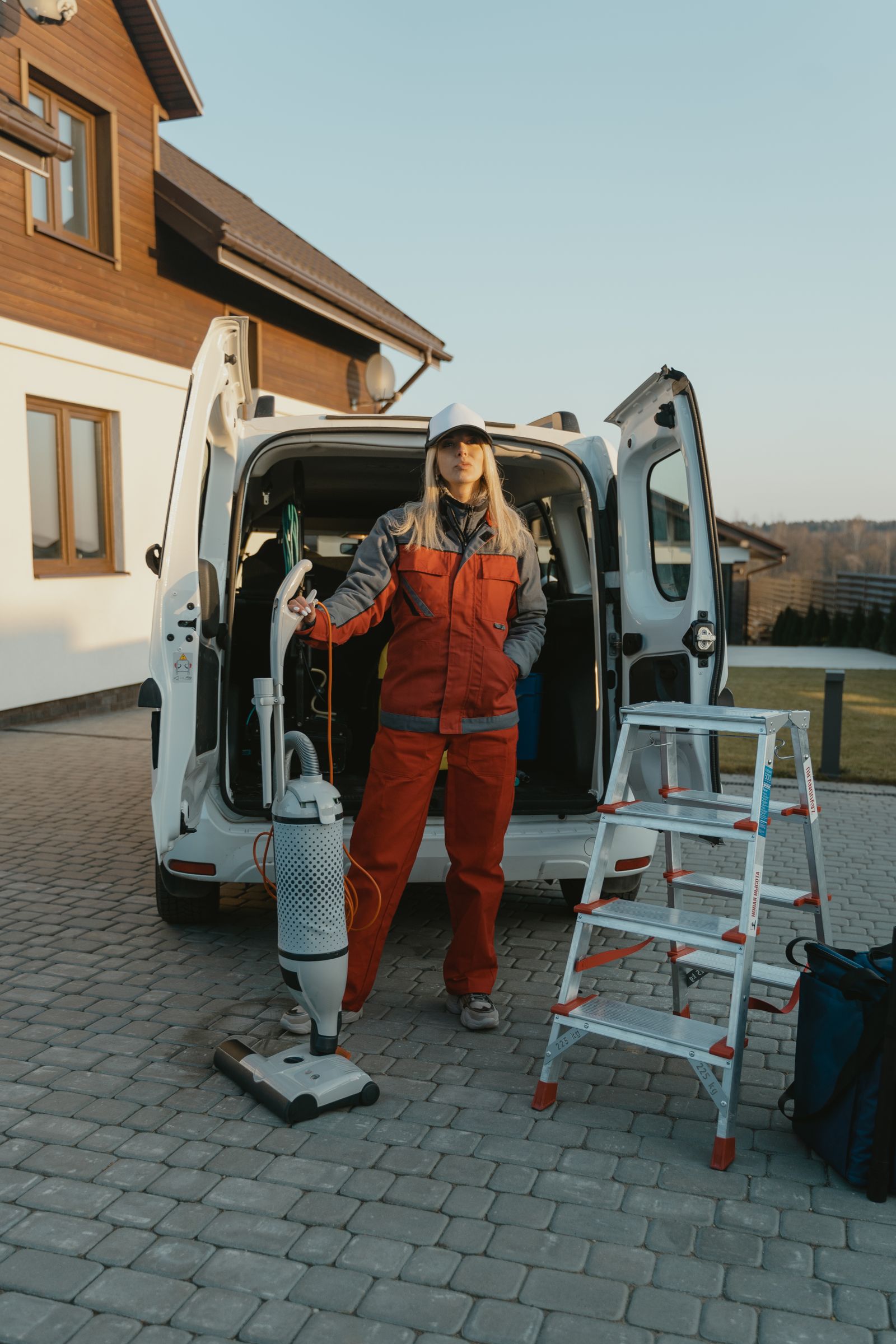 A uniformed cleaner standing beside a service van with equipment outside a house at sunset