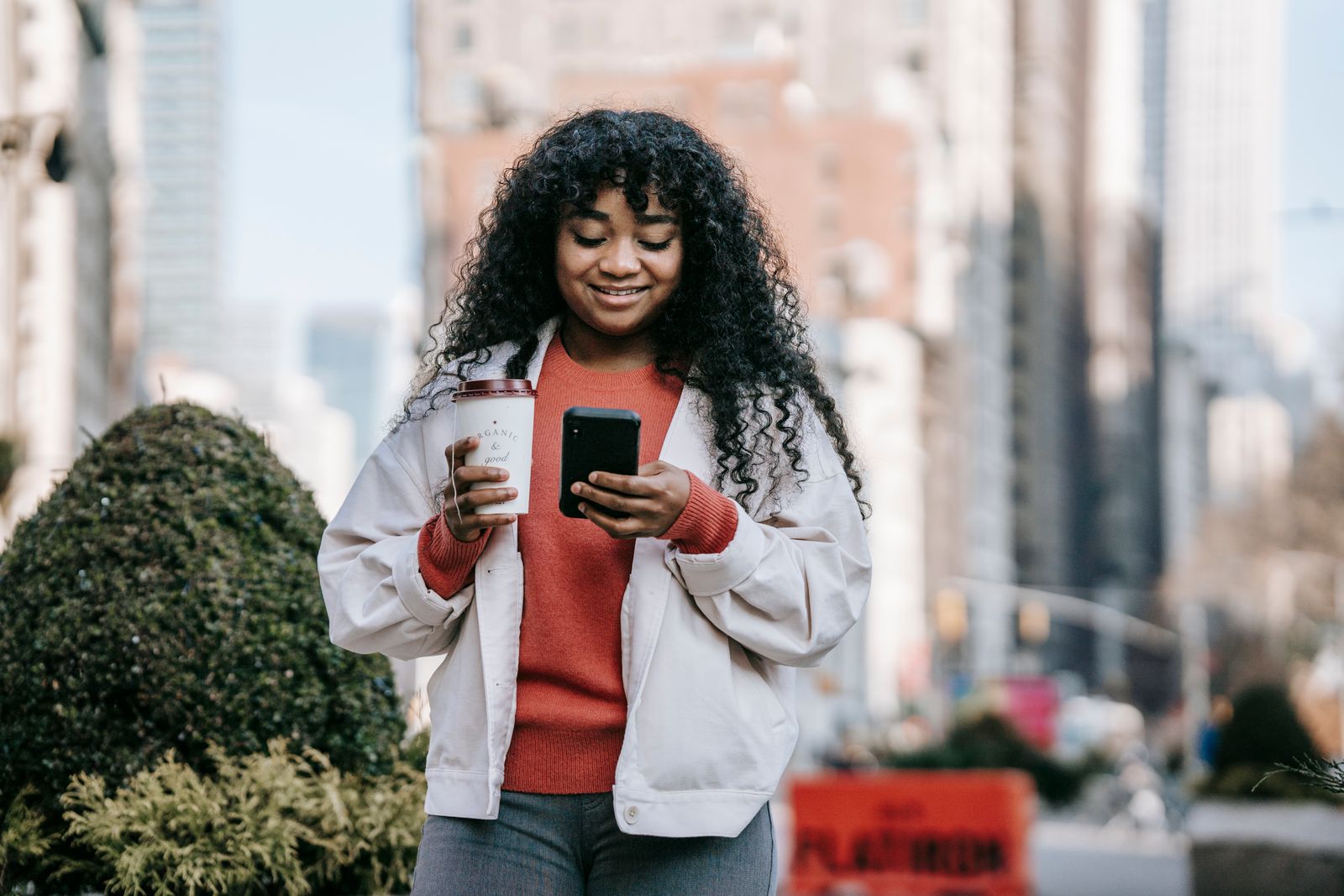 A person holding a coffee and using their smartphone on a city street